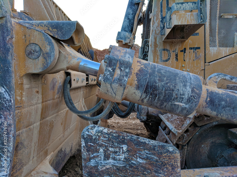 Muddy Caterpillar D11 Bulldozer - Hydraulic Actuator Detail at Sunset Muddy Caterpillar D11 Bulldozer - Hydraulic Actuator Detail at Sunset