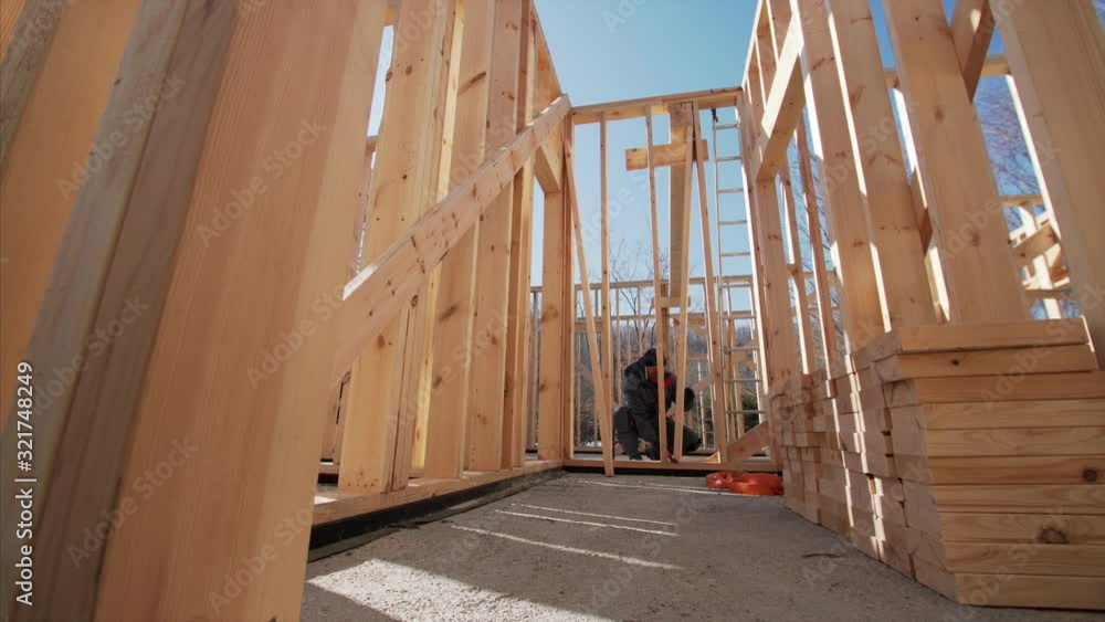 Sliding view from below of frame of future residential house: beams for walls, without second floor and ceiling, and builder. Sunny day Sliding view from below of frame of future residential house: beams for walls, without second floor and ceiling, and builder. Sunny day