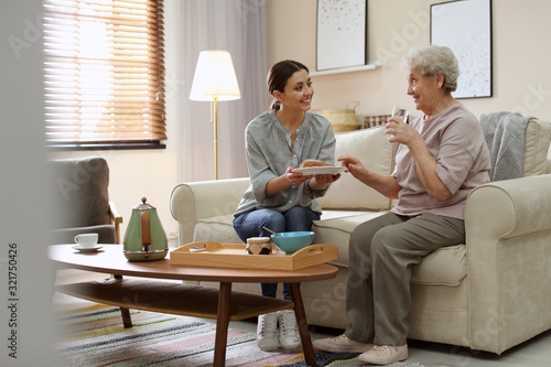 Obraz na plátně Young woman serving dinner for elderly woman in living room