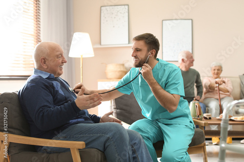 Care worker examining elderly patient with stethoscope in geriatric hospice