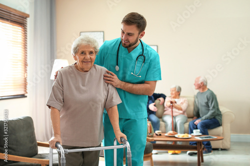 Care worker helping to elderly woman with walker in geriatric hospice