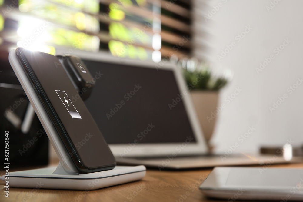 Mobile phone and smartwatch charging with wireless pad on wooden desk, space for text. Modern workplace device Mobile phone and smartwatch charging with wireless pad on wooden desk, space for text. Modern workplace device