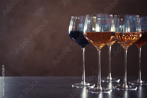 Elegant glasses with different wines on table against brown background