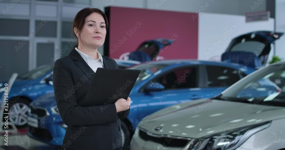 Portrait of Caucasian female car dealer standing in dealership with document holder and thinking. Serious businesswoman working in showroom. Auto industry, trading. Cinema 4k ProRes HQ. Portrait of Caucasian female car dealer standing in dealership with document holder and thinking. Serious businesswoman working in showroom. Auto industry, trading. Cinema 4k ProRes HQ.