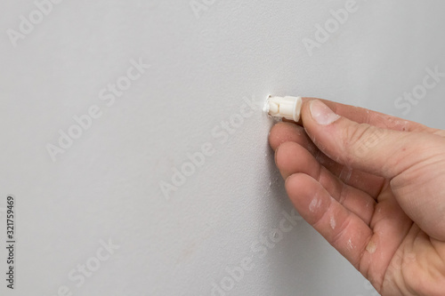 male hand pokes a plastic dowel into a white drywall wall photo
