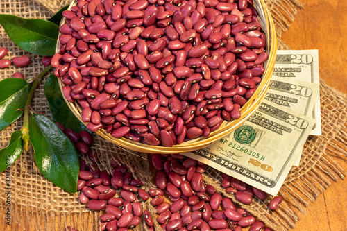 red Kidney dry beans in a small woven basket on an artesan weave fabric, twenty USD bills and wood background. zenith view.grains industry market concept photo