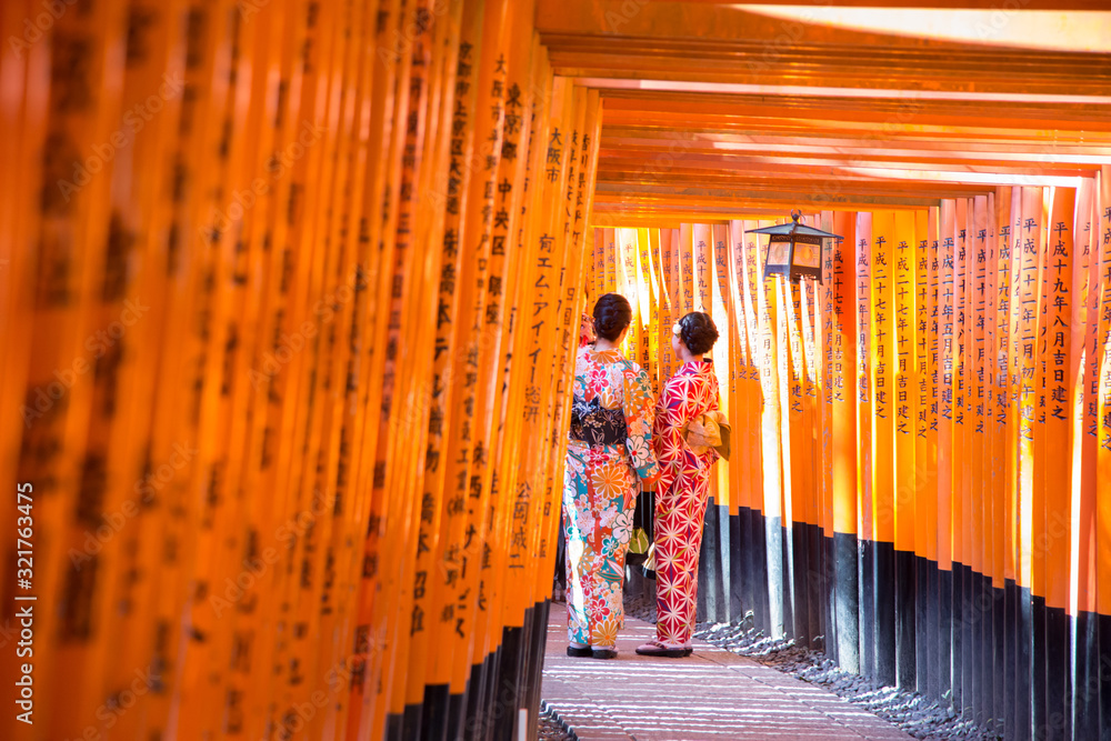 women geishas among red wooden Tori Gate at Fushimi Inari Shrine in Kyoto, Japan