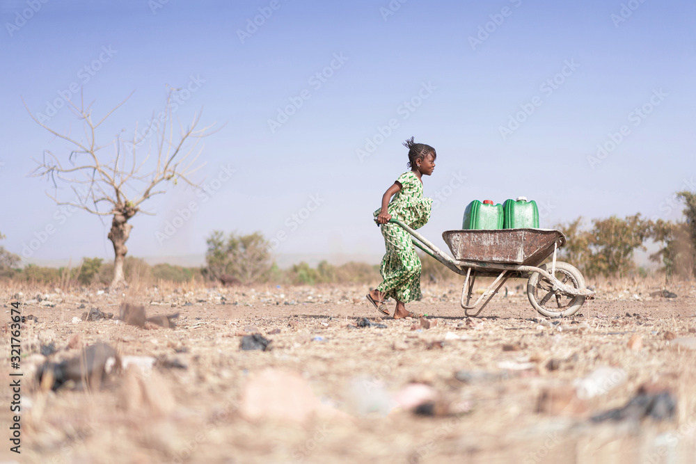 Fototapeta Little African Woman Transporting Fresh Water as a drought symbol