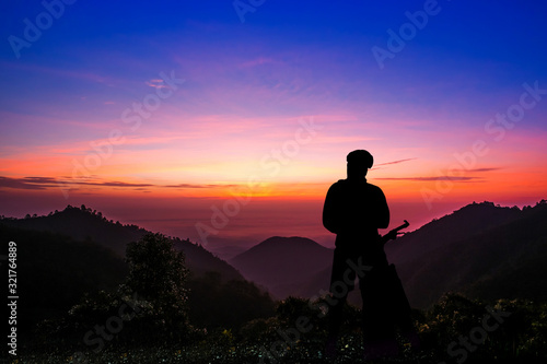 Silhouette of a young man with a bicycle at sunset sky with dramatic clouds on background