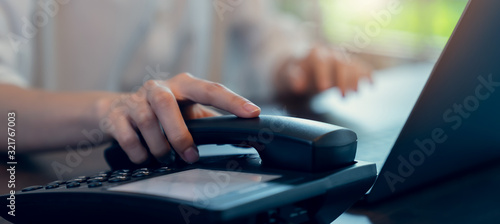 Woman hand holding the phone and working laptop on the office desk.