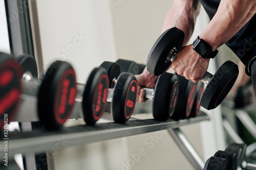 Close-up image of sportsman taking heavy dumbbell from rack