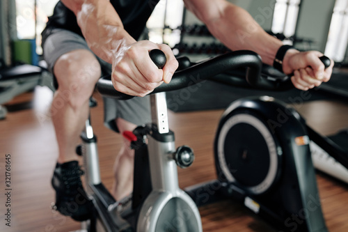 Cropped image of sportsman riding stationary bike in gym before working out