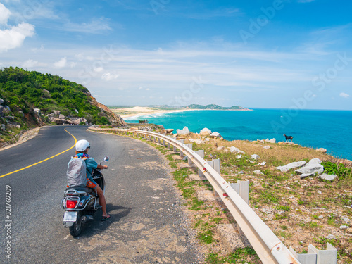 One person riding motorbike on winding road looking at view of gorgeous coast in the Phu Yen province, Nha Trang Quy Nhon, adventure traveling in Vietnam. Unique tropical bay and golden beach.