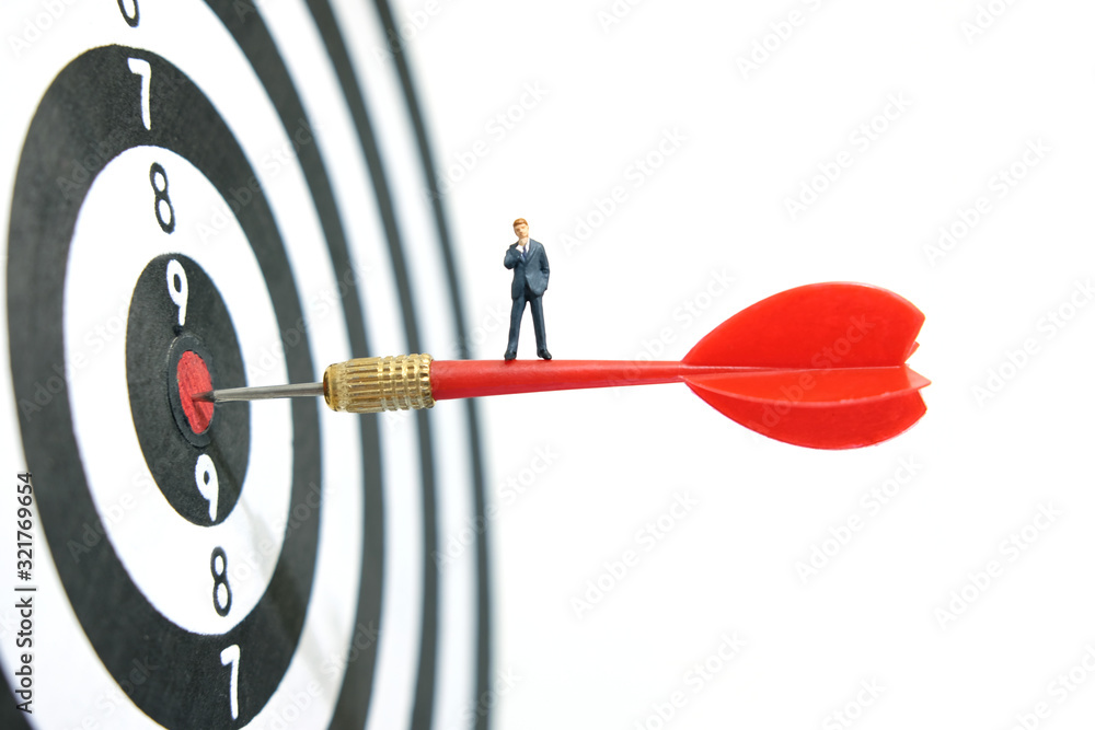 Business strategy conceptual photo - Miniature of businessman standing on red arrow which embedded on the center target Business strategy conceptual photo - Miniature of businessman standing on red arrow which embedded on the center target