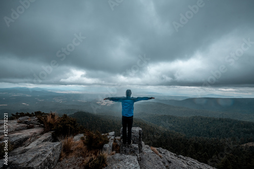 Fototapeta Naklejka Na Ścianę i Meble -  Adventurer on the edge of a cliff watching a wooded landscape, on a rocky mountain, rain clouds are seen in the background