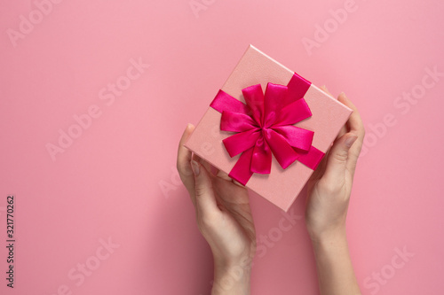 Fototapeta Naklejka Na Ścianę i Meble -  Valentine's Day celebration concept. A nice gift from a loved one. Box with a bow in female hands on a delicate pink background. Copy space. Flat lay.