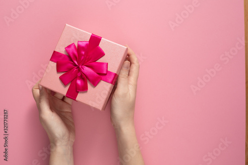 Valentine's Day celebration concept. A nice gift from a loved one. Box with a bow in female hands on a delicate pink background. Copy space. Flat lay. © Danil