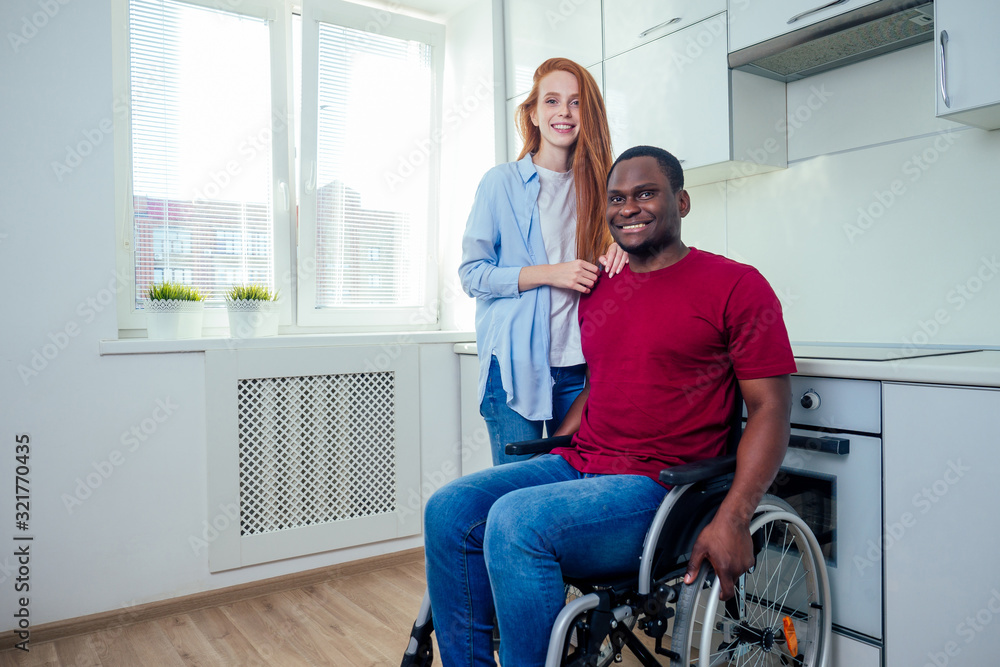 Young bearded handicapped african american man in wheelchair and his pretty wife at kichen Young bearded handicapped african american man in wheelchair and his pretty wife at kichen