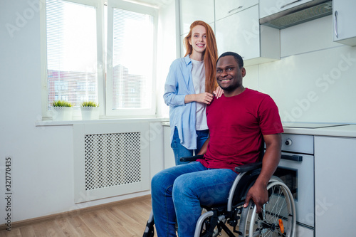 Young bearded handicapped african american man in wheelchair and his pretty wife at kichen