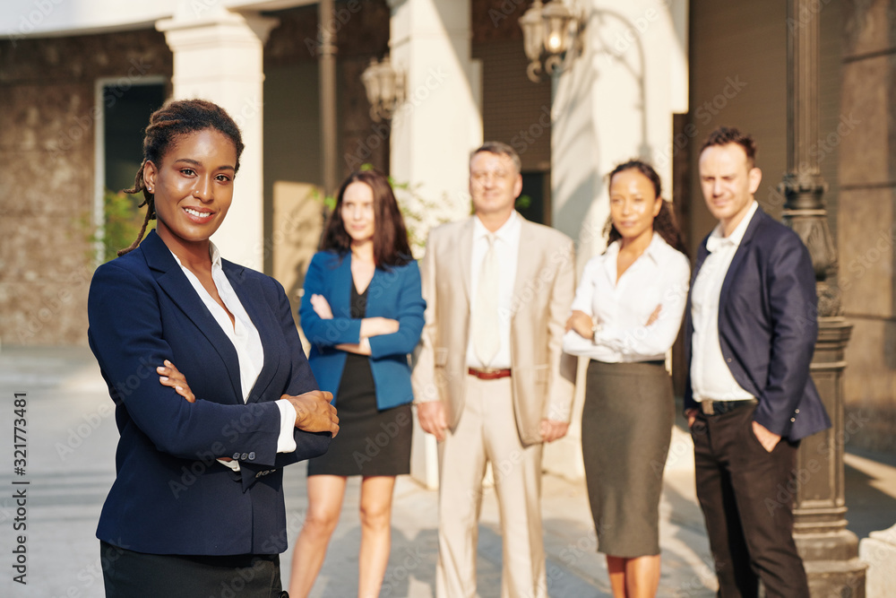 Portrait of pretty successful business lady with arms folded standing in front of her business team Portrait of pretty successful business lady with arms folded standing in front of her business team