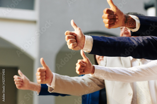 Hands of successful business people standing outdoors and showing thumbs-up