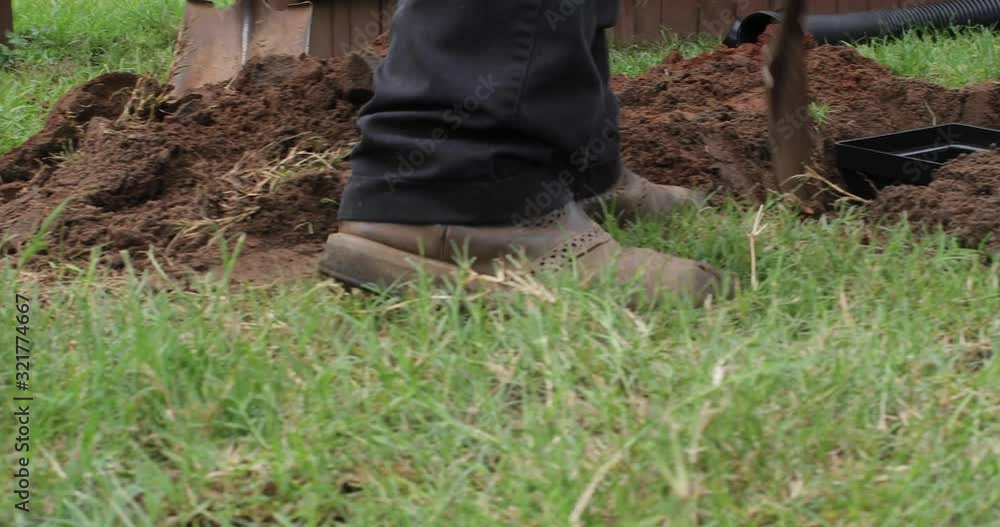 Worker digging out a trench to fit a new french drain pipe system in the ground Worker digging out a trench to fit a new french drain pipe system in the ground