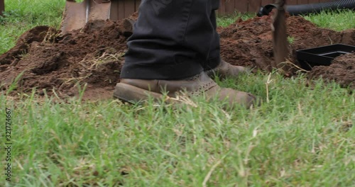 Worker digging out a trench to fit a new french drain pipe system in the ground