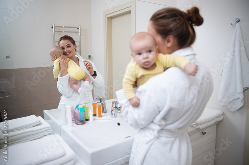 Happy woman brushing teeth and holding her baby stock photo