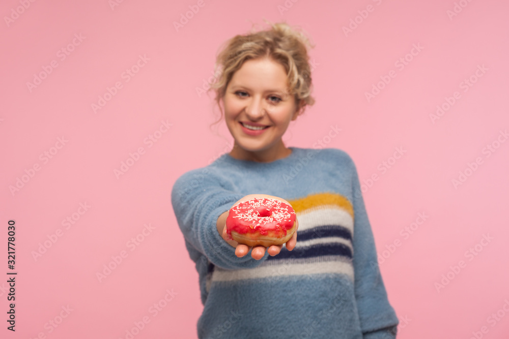 Take sweet donut! Portrait of happy adult woman with short hair in sweater giving doughnut to camera and smiling, offering tasty confection, dessert. indoor studio shot isolated on pink background Take sweet donut! Portrait of happy adult woman with short hair in sweater giving doughnut to camera and smiling, offering tasty confection, dessert. indoor studio shot isolated on pink background