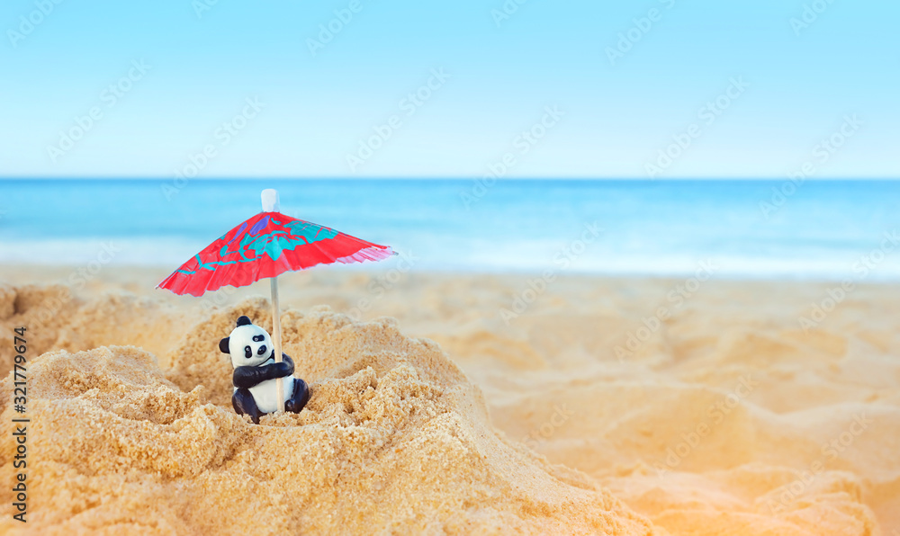 Obraz premium Panda on beach, weekend travel concept. cute panda toy with beach umbrella and sea coast. summer time, vacation. close up. copy space