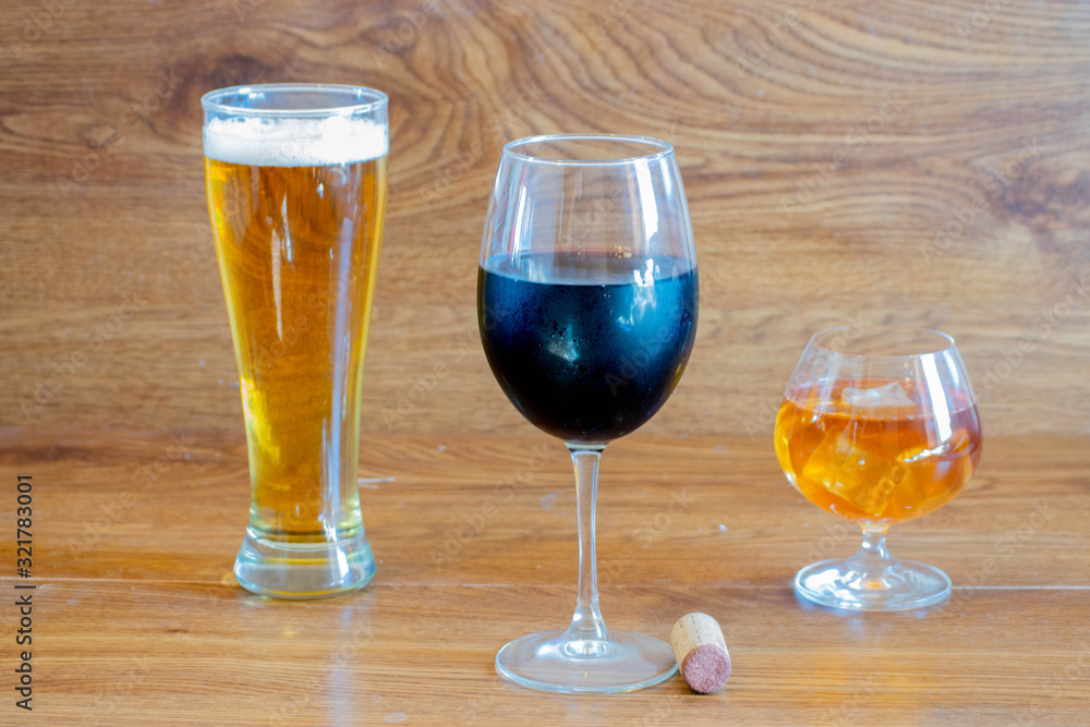 composition of alcoholic drinks with glass of whiskey, glass of clear beer and glass of red wine on stage of oak tables with a bottle cork composition of alcoholic drinks with glass of whiskey, glass of clear beer and glass of red wine on stage of oak tables with a bottle cork