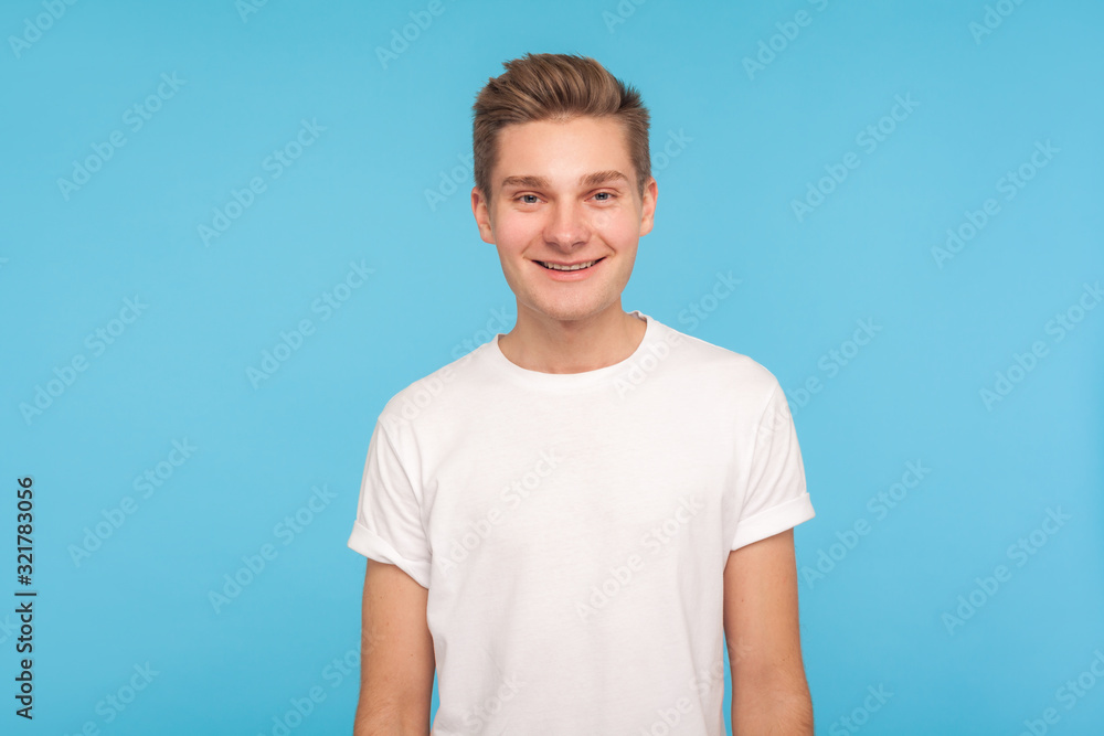 Portrait of handsome happy friendly guy in casual white t-shirt standing, smiling to camera with kind good-natured amiable expression, optimistic mood. indoor studio shot isolated on blue background Portrait of handsome happy friendly guy in casual white t-shirt standing, smiling to camera with kind good-natured amiable expression, optimistic mood. indoor studio shot isolated on blue background