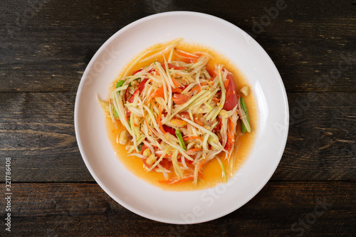 Papaya salad with chili and lemon in white dish on wooden table. Som Tam Thai 