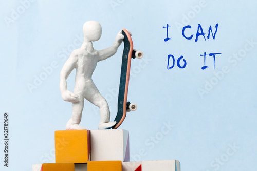 A man in white plasticine is standing on top of cubes on a blue background and holding a skateboard in one hand. concept of motivation, success, achievement of the set goal..