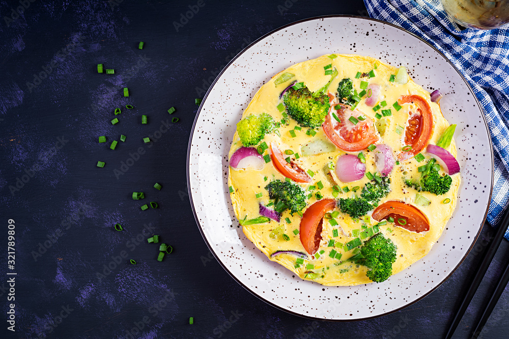 Omelette with broccoli, tomatoes and red onions on dark table. Italian frittata with vegetables. Top view, overhead Omelette with broccoli, tomatoes and red onions on dark table. Italian frittata with vegetables. Top view, overhead