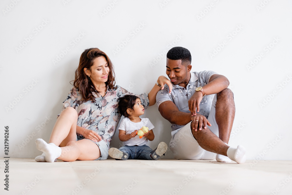 Young loving family asian mom african-american dad and mixed race daughter sit on floor at home resting at weekend. Concept of happy young loving and caring family. Understanding Parents and Children Young loving family asian mom african-american dad and mixed race daughter sit on floor at home resting at weekend. Concept of happy young loving and caring family. Understanding Parents and Children
