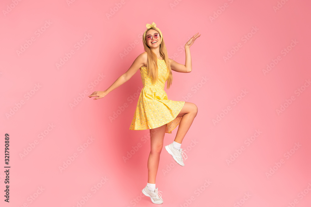 Cheerful woman dancing jumping over pink studio wall