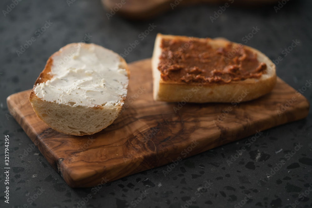 Toasted half of ciabatta with cream cheese and red pesto on olive board