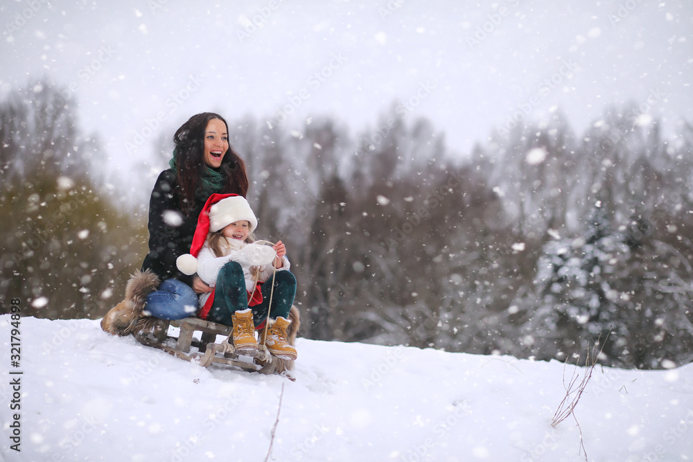 A winter fairy tale, a young mother and her daughter. A girl on a sled with gifts on the eve of the new year in the park. Two sisters walk in a New Year's park and ride a sled with gifts. A winter fairy tale, a young mother and her daughter. A girl on a sled with gifts on the eve of the new year in the park. Two sisters walk in a New Year's park and ride a sled with gifts.