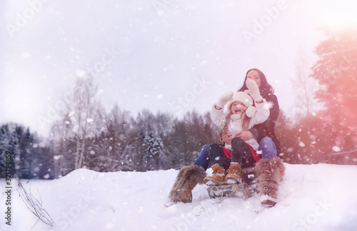 A winter fairy tale, a young mother and her daughter. A girl on a sled with gifts on the eve of the new year in the park. Two sisters walk in a New Year's park and ride a sled with gifts.