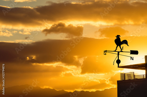 Silhouette of weather vane for wind direction, decorative metallic rooster at colorful dawn. No AI tools were used.  Creative collage, my own photos and traditional digital enhancement tools were used
