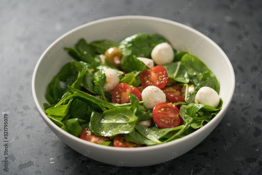 Salad with cherry tomatoes, spinach leaves and mozzarella balls in white bowl on terrazzo surface Salad with cherry tomatoes, spinach leaves and mozzarella balls in white bowl on terrazzo surface