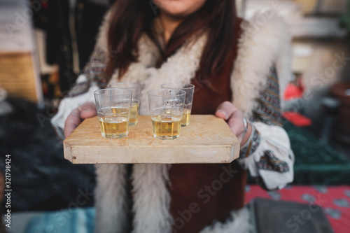 Photos Shallow depth of field (selective focus) image with a woman holding a wooden plate with palinca (or tuica), romanian traditional plum brandy