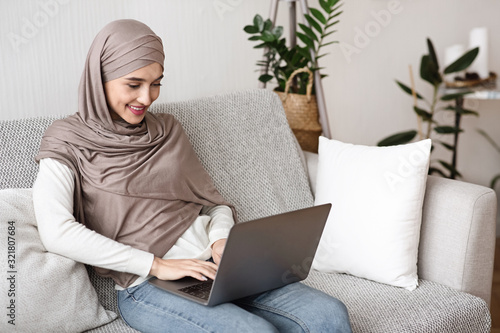 Young muslim woman in hijab using laptop computer at home