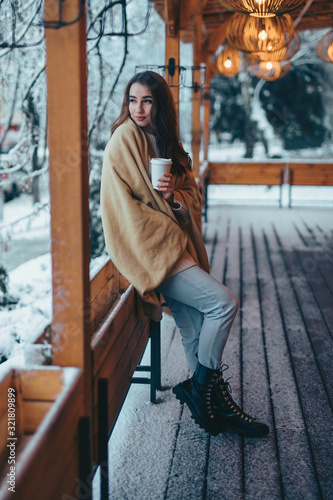 Woman holding paper coffee cup standing on beautiful cafe terrace at winter day