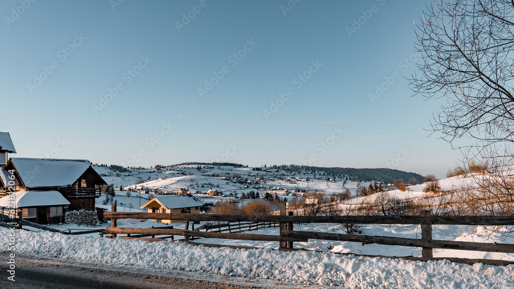 Winter season, landscape picture of a village covered by snow at sunset, country landscape with timber fence