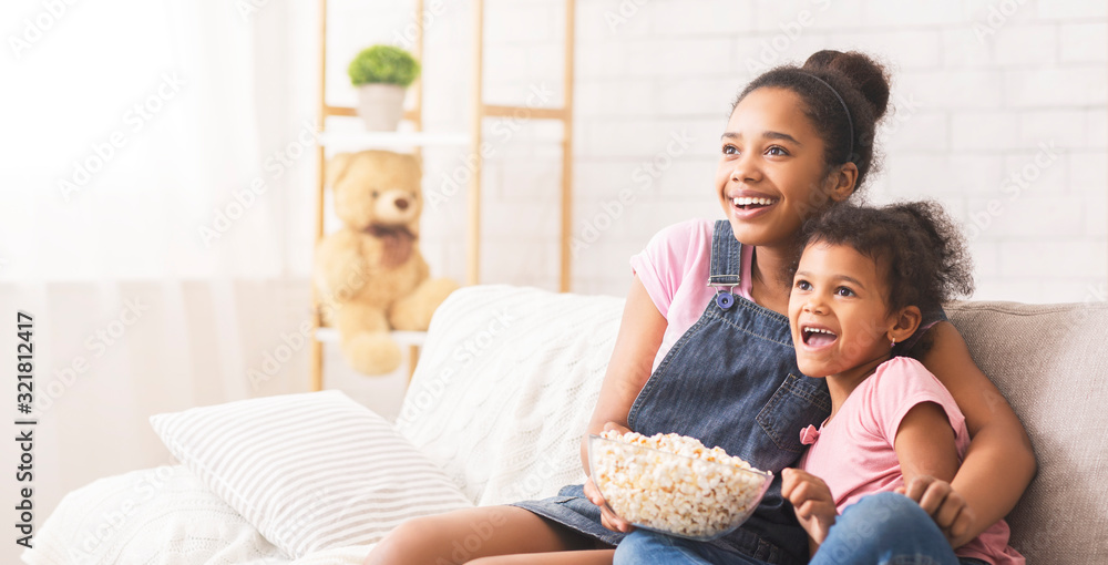 Two emotional african sisters watching tv and eating popcorn Two emotional african sisters watching tv and eating popcorn