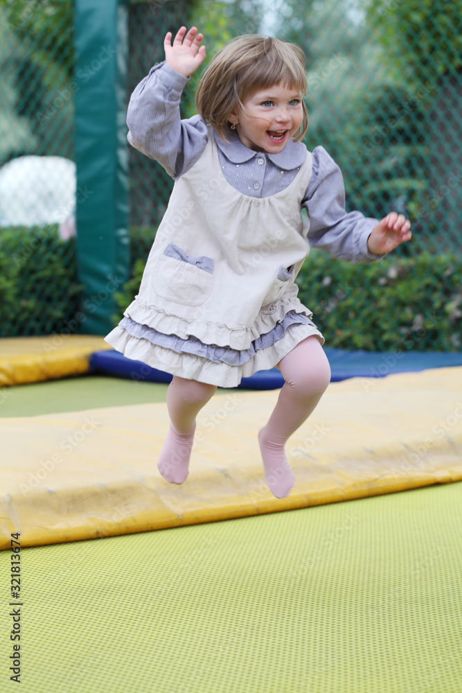 Fototapeta premium Little girl on playground in a park, jumping on trampoline Little Girl on a Trampoline.