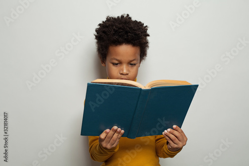 Serious black kid boy reading a book on white background