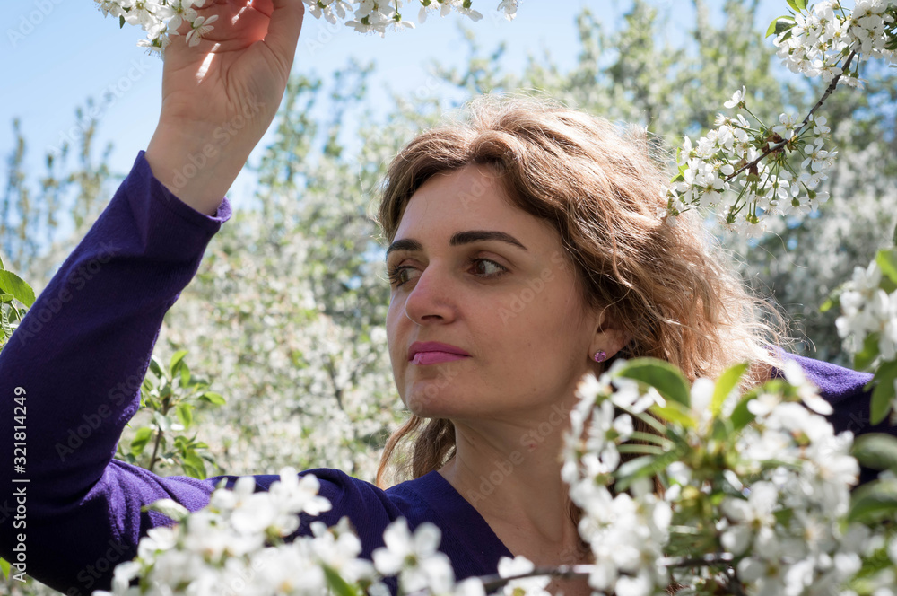 Obraz premium soft focus of beautiful confident woman between white flowers on tree looking away and holding blossoming branch in garden in front of blue sky